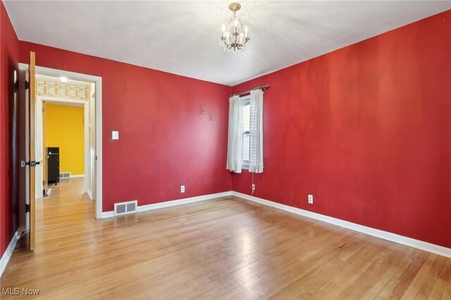 empty room featuring visible vents, baseboards, a chandelier, and hardwood / wood-style floors