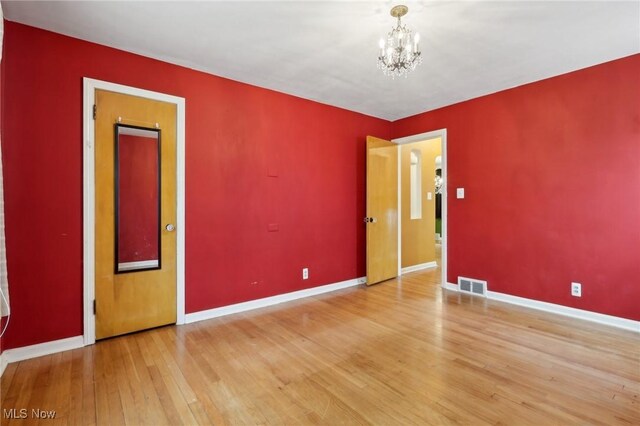 empty room featuring baseboards, a chandelier, visible vents, and hardwood / wood-style floors