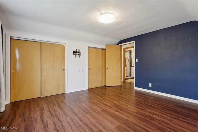 unfurnished bedroom with baseboards, multiple closets, wood finished floors, and vaulted ceiling