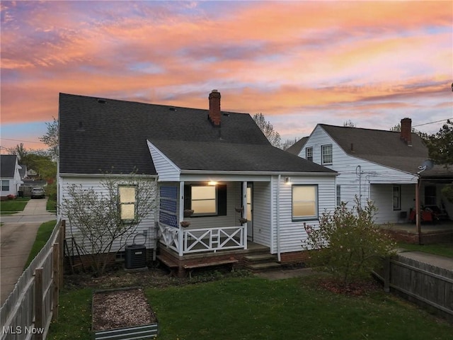 back of house at dusk featuring central AC, a chimney, covered porch, a yard, and fence private yard