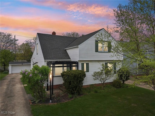 view of front of house featuring a front lawn, roof with shingles, a chimney, an outbuilding, and a detached garage