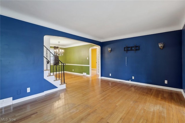 unfurnished living room featuring arched walkways, stairway, baseboards, a notable chandelier, and hardwood / wood-style floors