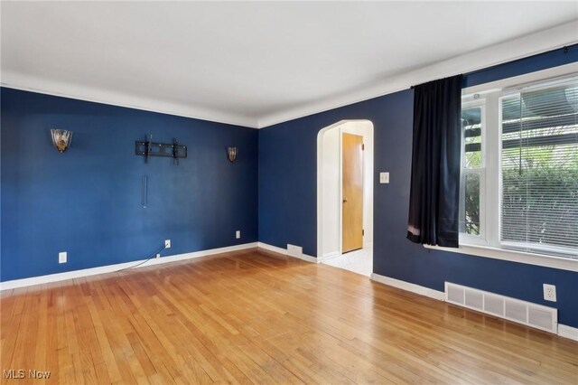empty room featuring visible vents, arched walkways, wood-type flooring, and baseboards