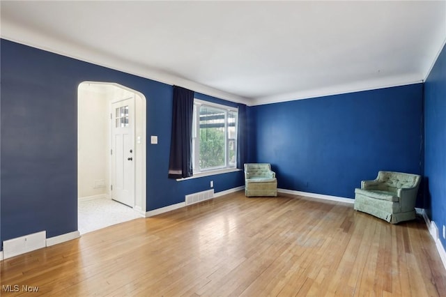 unfurnished room with visible vents, arched walkways, baseboards, and hardwood / wood-style flooring