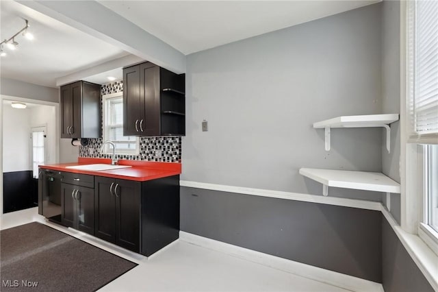 kitchen featuring open shelves, a sink, rail lighting, black dishwasher, and decorative backsplash