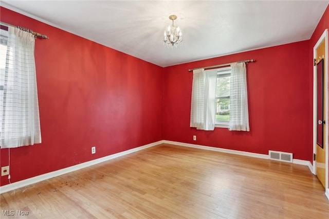 unfurnished room featuring visible vents, baseboards, wood finished floors, and a notable chandelier