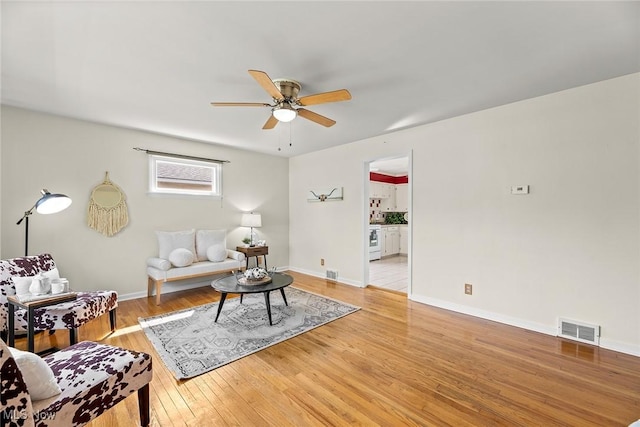 living room featuring baseboards, ceiling fan, light wood finished floors, and visible vents