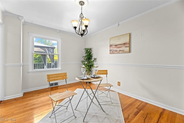 dining room featuring crown molding, a chandelier, baseboards, wood finished floors, and visible vents
