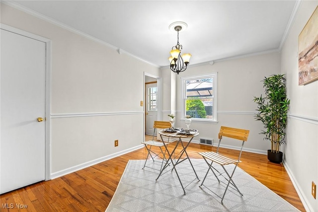 dining area featuring crown molding, a notable chandelier, visible vents, and wood finished floors
