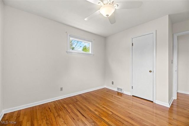 empty room featuring light wood-style floors, a ceiling fan, baseboards, and visible vents