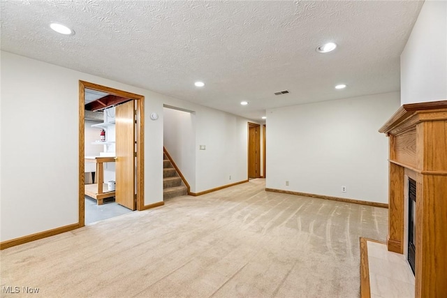 unfurnished living room featuring recessed lighting, a fireplace with flush hearth, light carpet, and stairway