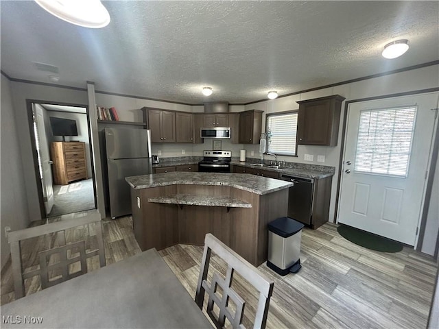 kitchen with appliances with stainless steel finishes, a center island, light wood-type flooring, dark brown cabinets, and a sink