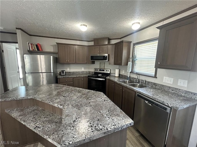 kitchen with wood finished floors, a center island, a textured ceiling, a sink, and stainless steel appliances