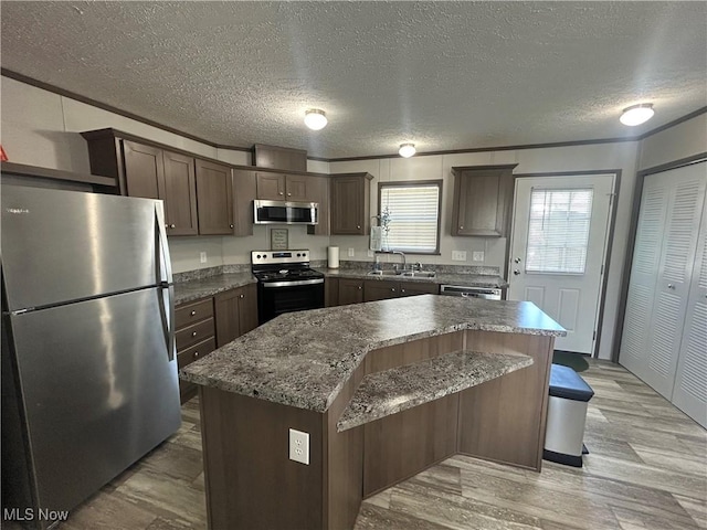 kitchen featuring dark brown cabinets, light wood-style floors, a textured ceiling, a sink, and appliances with stainless steel finishes