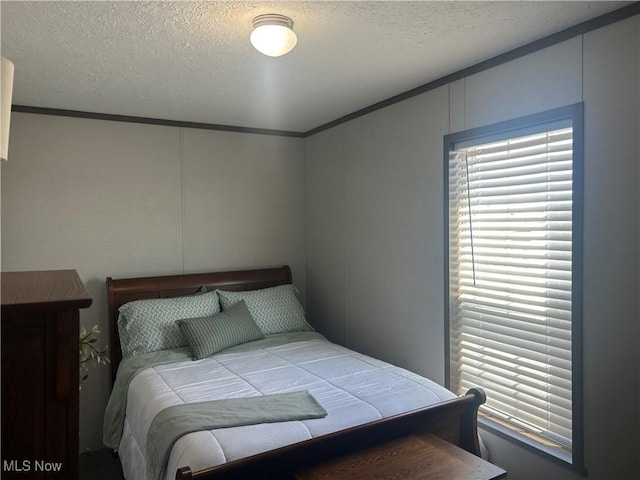 bedroom with a textured ceiling, ornamental molding, and a decorative wall