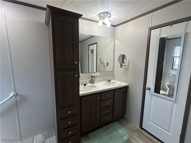 full bath with a sink, crown molding, double vanity, and wood finished floors