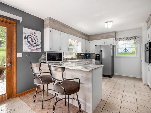 kitchen featuring stainless steel fridge with ice dispenser, a peninsula, tasteful backsplash, a sink, and light tile patterned floors
