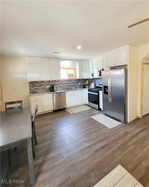 kitchen featuring white cabinets, appliances with stainless steel finishes, dark wood finished floors, tasteful backsplash, and visible vents
