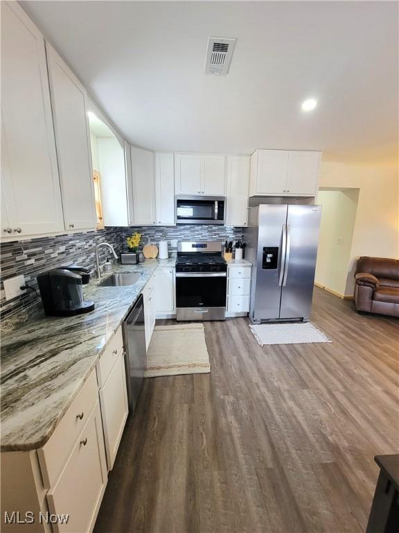 kitchen with light stone countertops, a sink, stainless steel appliances, white cabinetry, and dark wood-style floors