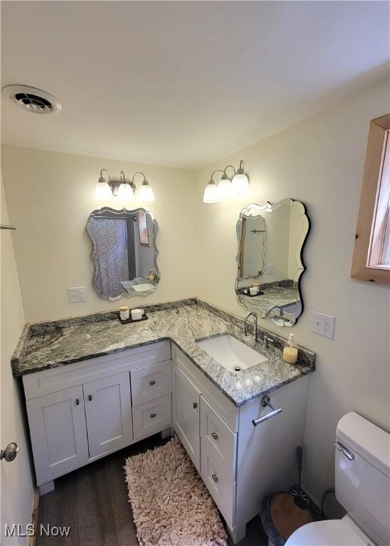 bathroom with vanity, toilet, wood finished floors, and visible vents