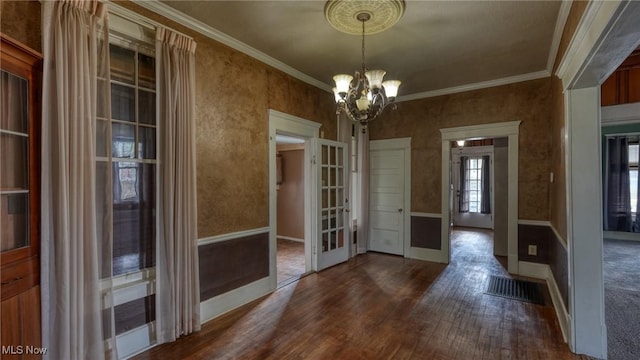 unfurnished dining area featuring french doors, visible vents, a chandelier, ornamental molding, and dark wood-type flooring