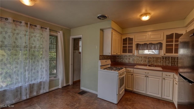 kitchen featuring a sink, gas range gas stove, freestanding refrigerator, decorative backsplash, and glass insert cabinets