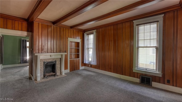 unfurnished living room with a healthy amount of sunlight, carpet floors, wood walls, and visible vents