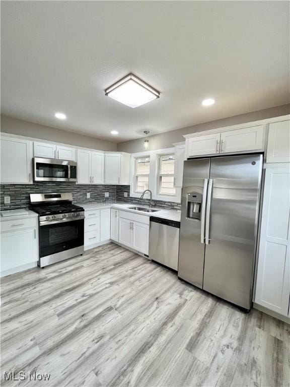 kitchen with white cabinetry, tasteful backsplash, a sink, light wood-style flooring, and stainless steel appliances