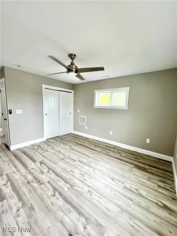 unfurnished bedroom featuring visible vents, a closet, wood finished floors, baseboards, and ceiling fan