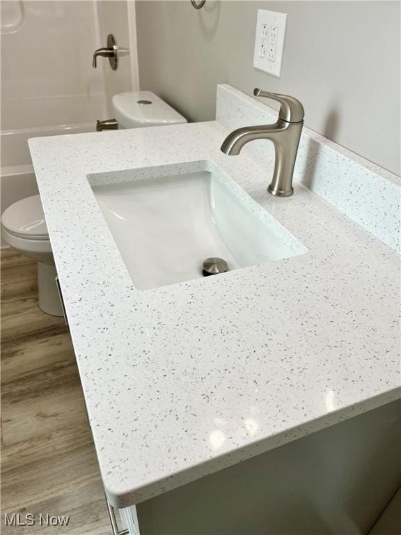 interior details featuring vanity, a washtub, toilet, and wood finished floors