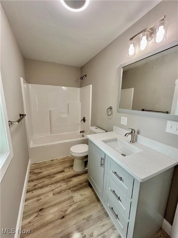 bathroom with shower / bathtub combination, toilet, wood finished floors, and vanity