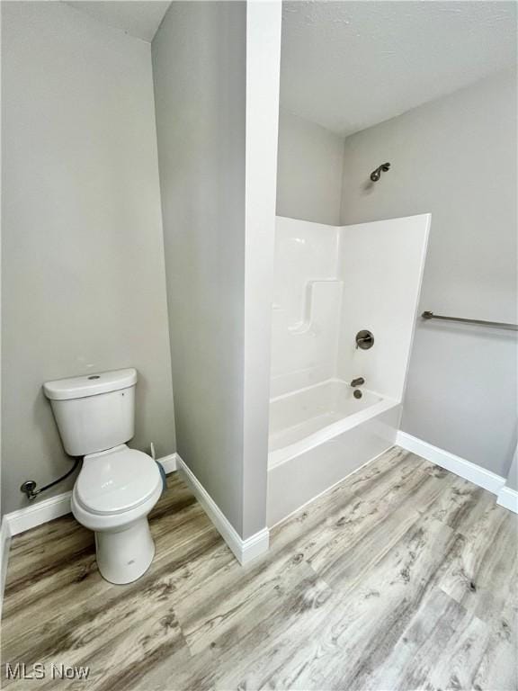 bathroom featuring baseboards, toilet, wood finished floors, and shower / tub combination