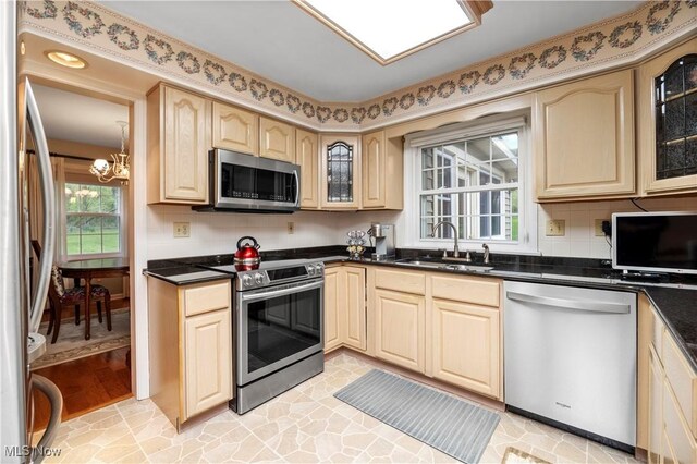 kitchen with appliances with stainless steel finishes, glass insert cabinets, a sink, and an inviting chandelier