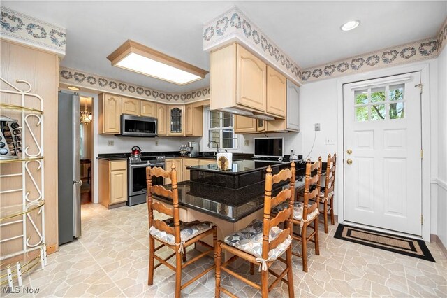 kitchen with light brown cabinets, stone finish floor, dark countertops, and stainless steel appliances