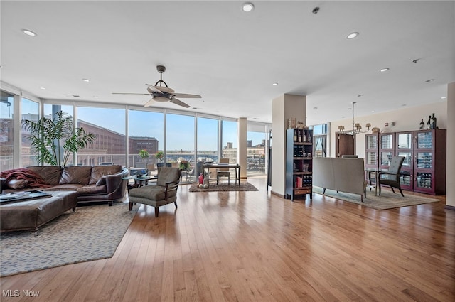 living room featuring recessed lighting, a wall of windows, ceiling fan with notable chandelier, and light wood-style floors