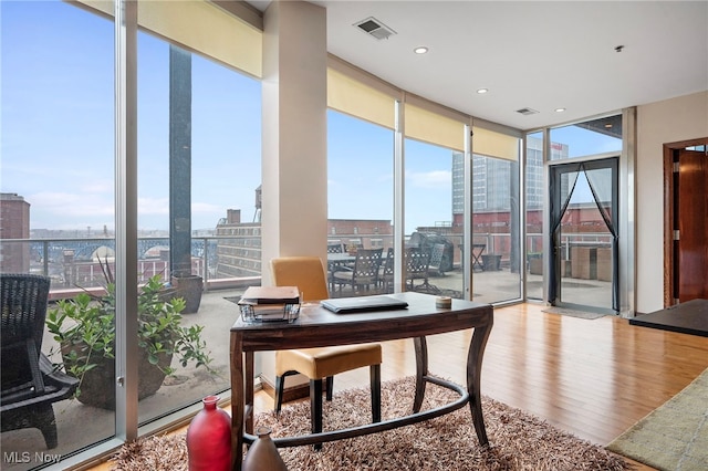 office with a view of city, floor to ceiling windows, wood finished floors, and visible vents