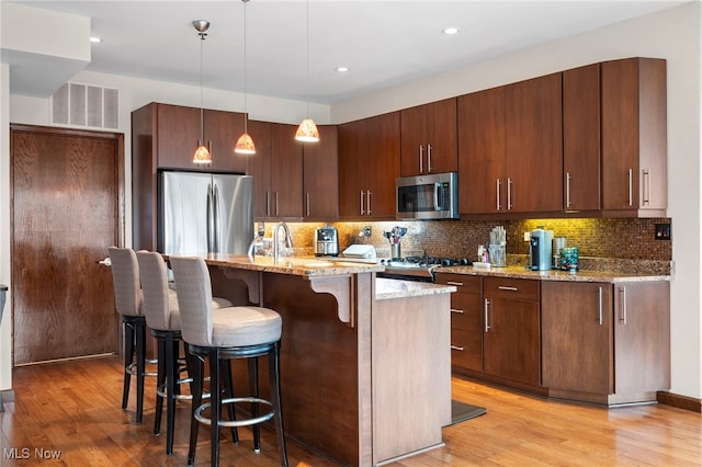 kitchen featuring visible vents, light stone countertops, a kitchen breakfast bar, light wood-type flooring, and appliances with stainless steel finishes