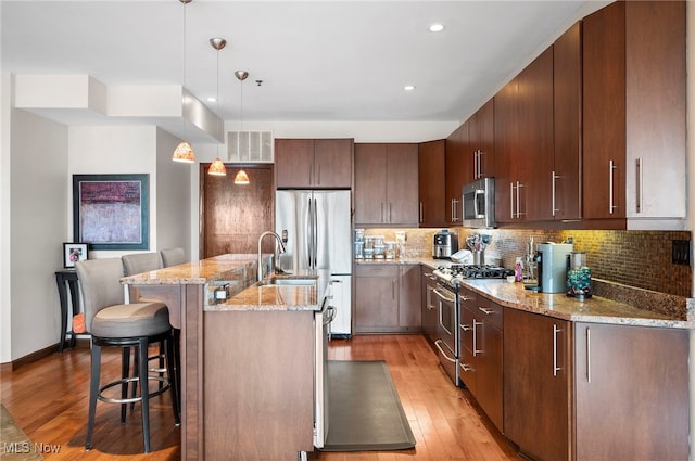 kitchen with a kitchen breakfast bar, backsplash, appliances with stainless steel finishes, light stone countertops, and light wood-style floors