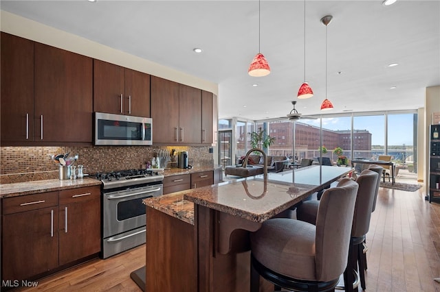 kitchen with stone countertops, open floor plan, a breakfast bar area, light wood-type flooring, and appliances with stainless steel finishes