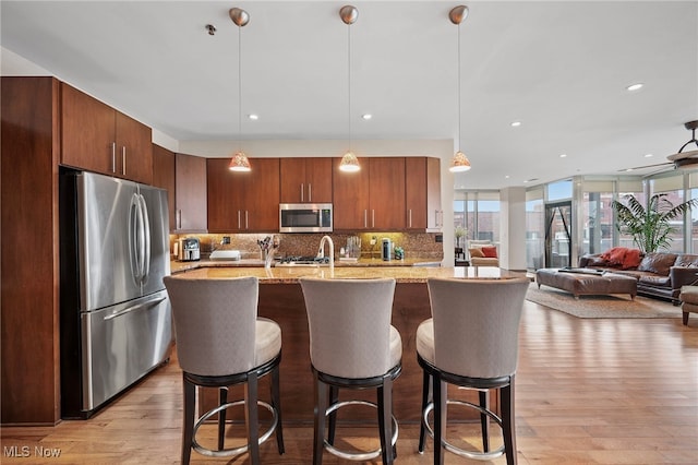 kitchen featuring stainless steel appliances, a kitchen bar, light wood finished floors, and tasteful backsplash