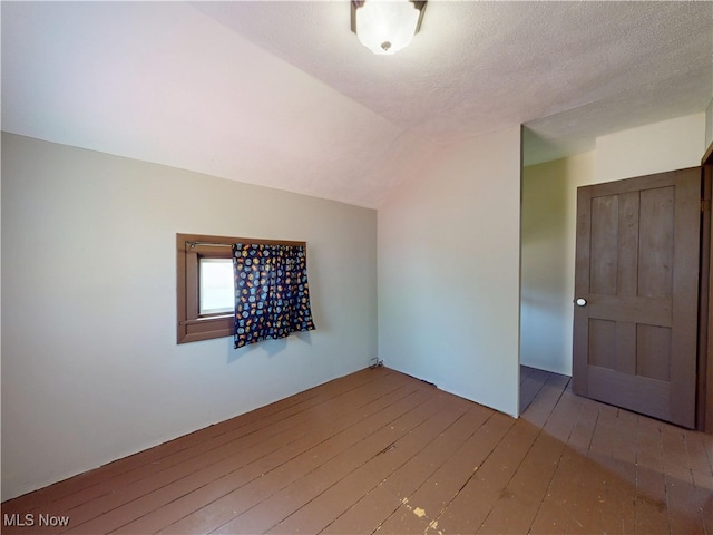 spare room with wood-type flooring and lofted ceiling
