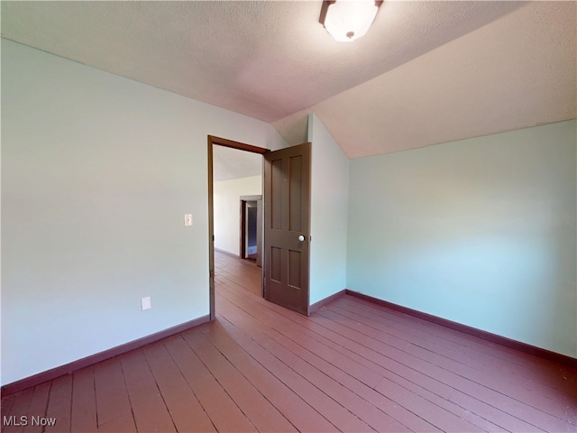 spare room featuring light wood-style floors, baseboards, a textured ceiling, and lofted ceiling