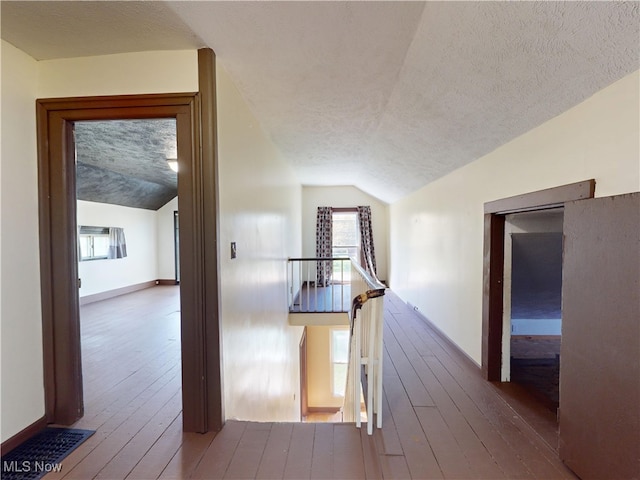additional living space with a healthy amount of sunlight, wood-type flooring, vaulted ceiling, and a textured ceiling