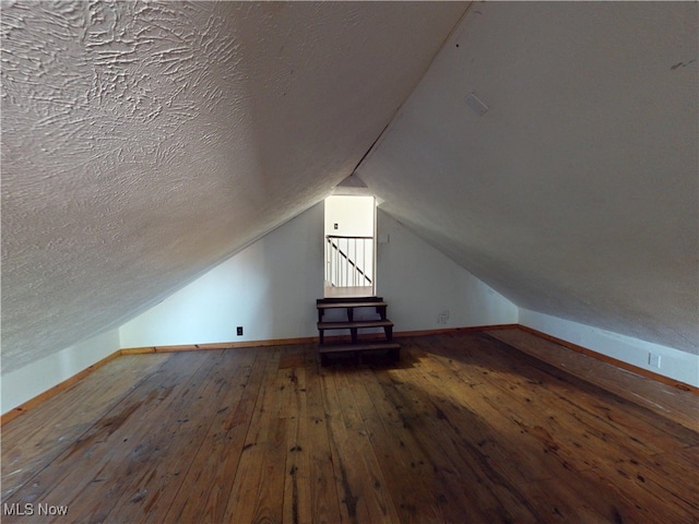 additional living space with baseboards, a textured ceiling, vaulted ceiling, and hardwood / wood-style flooring