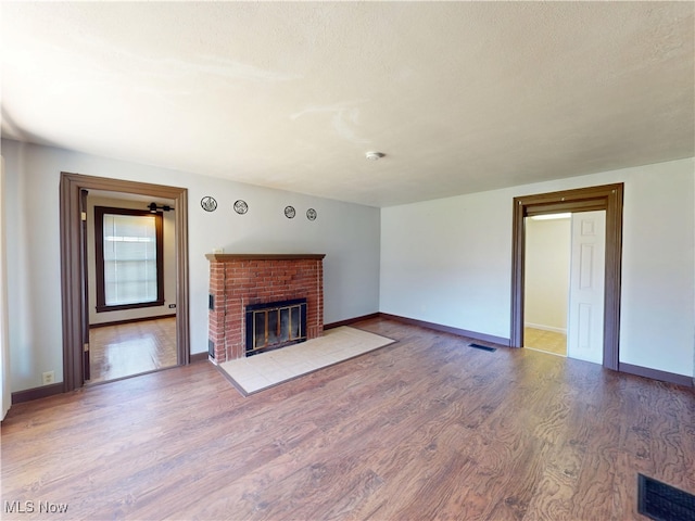 unfurnished living room with baseboards, visible vents, wood finished floors, and a fireplace