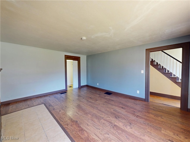 unfurnished room featuring baseboards, stairs, wood finished floors, and visible vents