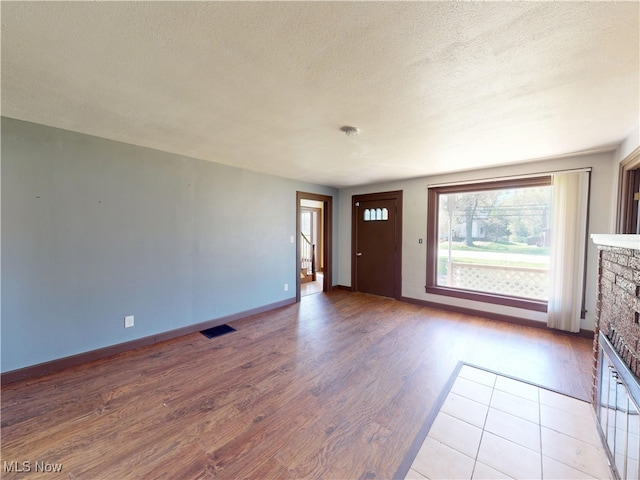 interior space featuring a fireplace, a textured ceiling, baseboards, wood finished floors, and visible vents