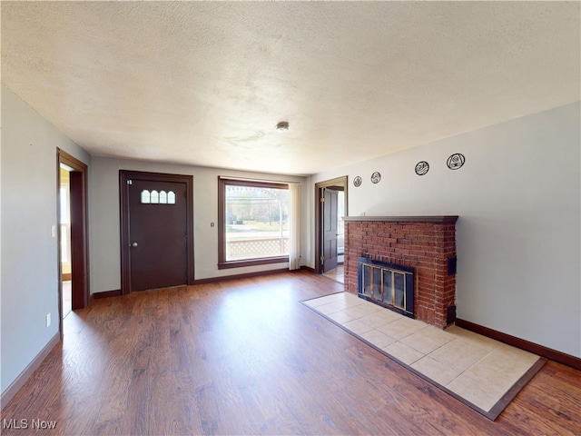 unfurnished living room featuring a brick fireplace, a textured ceiling, baseboards, and wood finished floors