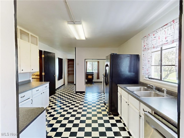 kitchen with plenty of natural light, stainless steel dishwasher, a sink, tile patterned floors, and white cabinetry