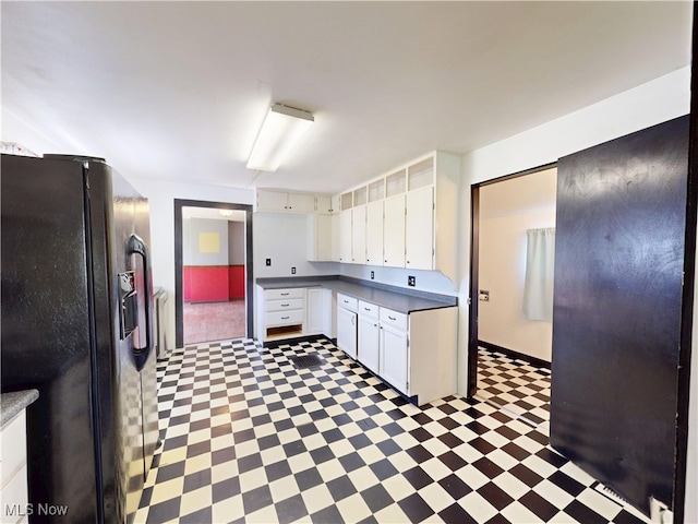 kitchen with white cabinetry, baseboards, light floors, and black fridge with ice dispenser